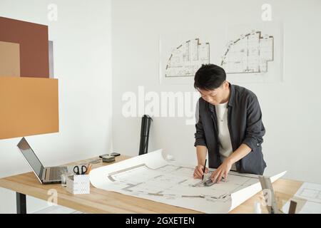 Junge Architektin zeichnet eine Skizze der Konstruktion, während sie sich über den Arbeitsplatz beugt Stockfoto