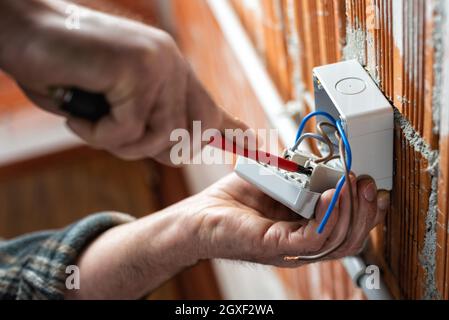 Ansicht von unten. Elektriker mit einem Schraubendreher fixiert das Kabel in der Klemme des Schalters einer elektrischen Anlage. Bauindustrie. Stockfoto