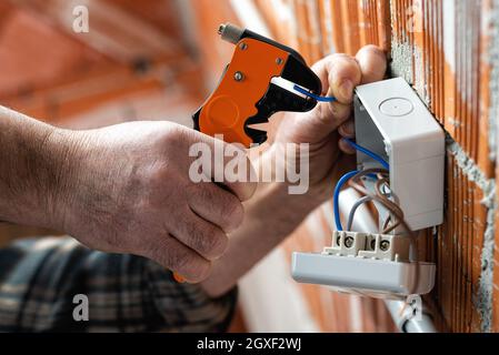 Ansicht von unten. Elektriker bei der Arbeit mit Abisolierer bereitet die elektrischen Kabel eines elektrischen Systems. Bauindustrie. Stockfoto