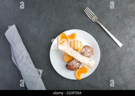 Karnevalsbonbons auf einem weißen Teller auf schwarzem Hintergrund serviert. Sfrappole oder chiacchiere oder Engelsflügel. Castagnole, ein Teig gebraten und bedeckt wi Stockfoto