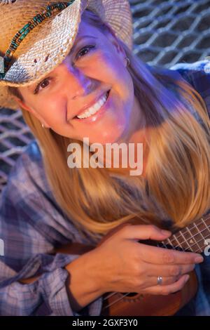 Schönen Abend Portrait Cowgirl in der Nähe von Lagerfeuer ihrer Ukulele zu spielen. Stockfoto