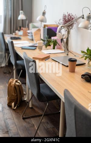 Langer Holzschreibtisch mit Lampen und Stühlen, die in einem modernen Büro an der Wand stehen Stockfoto