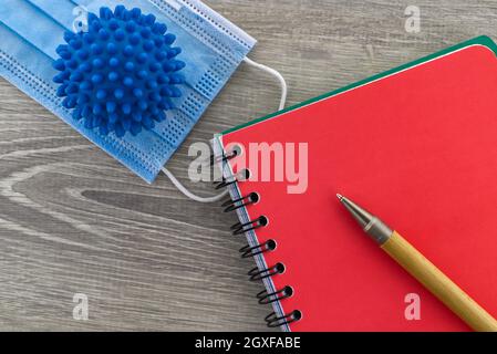 Symptome von Coronavirus und medizinisches Konzept mit einem chirurgischen Gesicht Maske mit einem Corona-Virus-Modell neben einem Draht gebunden Notizblock und Stift Stockfoto