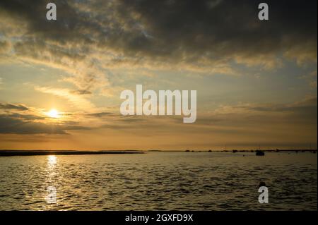 Dramatischer Himmel mit Sonnenuntergang über der Nordseeküste in der Nähe von Blakeney Point mit Booten in Silhouette, die auf dem Wasser, Norfolk, England, vertäut sind. Stockfoto