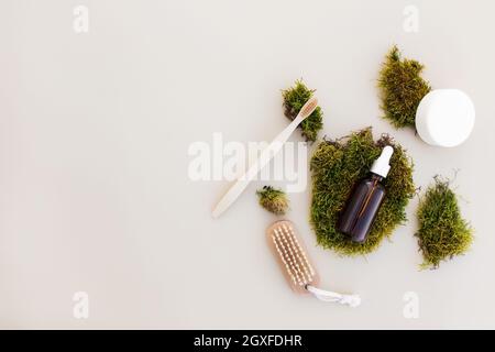 Healthcare Konzept der Bad-Accessoires Flay Lay mit einer Flasche ätherisches Öl, Holzzahnbürste, Fußbürste, Seife auf beigem Hintergrund und grünem Moos a Stockfoto