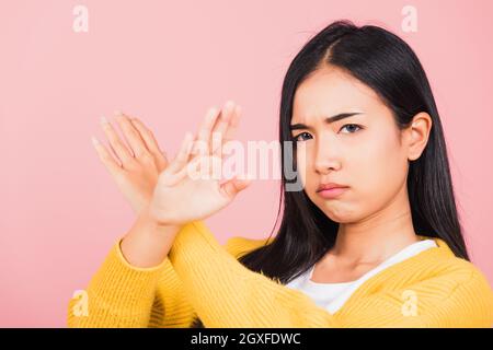 Portrait Asian schöne junge Frau unglücklich oder selbstbewusst stehende tragen halten zwei Kreuzarme sagen kein X-Zeichen, Studio Schuss isoliert rosa Hintergrund, Th Stockfoto