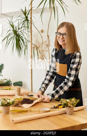 Lächelnde Floristin Frau macht schöne Bouquet von getrockneten Blumen auf Holztisch Stockfoto