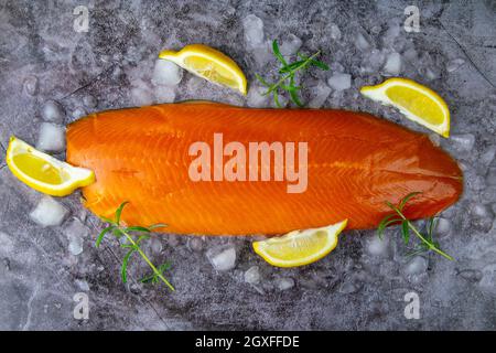 Frisches, rohes Lachsfischsteak mit Gewürzen auf Eis auf dunklem Steingrund. Kreatives Layout aus Fisch, Draufsicht, Flachlage Stockfoto