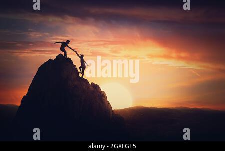 Blick auf die Landschaft mit einem Team von zwei Bergsteigern auf der Spitze des Berges. Person, die einem anderen hilft, Hindernisse zu überwinden und gemeinsam die Spitze zu erreichen. Teamarbeit Stockfoto