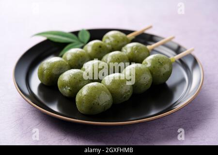 Beifuß-Reisknödel auf einem schwarzen Teller serviert, der vor einem violetten Hintergrund gestellt wird. Stockfoto