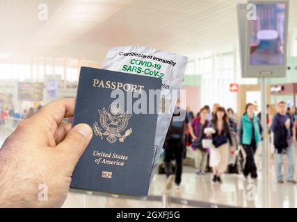 Hand hält einen US-Pass mit einem faltigen Papier Coronavirus Covid 19 Immunitätszertifikat verschwommen Flughafen im Hintergrund. Immunität gegen Covid-19. Stockfoto