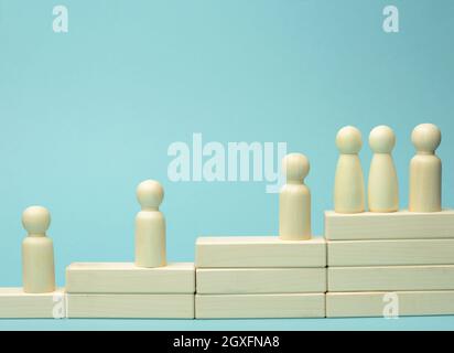 Holzfiguren von Männern auf einer Leiter aus Blöcken. Das Konzept der beruflichen Weiterentwicklung, Start bei der Arbeit, Ziele zu erreichen. Blauer Hintergrund Stockfoto