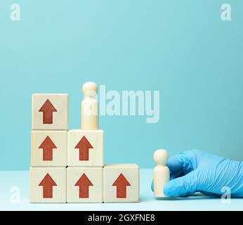 Holzfiguren von Männern auf einer Leiter aus Blöcken. Das Konzept der beruflichen Weiterentwicklung, Start bei der Arbeit, Ziele zu erreichen. Blauer Hintergrund Stockfoto