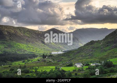 Kleines Ferienhaus umgeben von Wald, See und Fluss im Black Valley. MacGillycuddys Reeks Berge von Sonnenlicht beleuchtet, Ring of Kerry, Irland Stockfoto