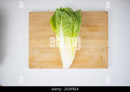 Romaine-Salat auf Holzschneidebrett über weißem Tisch. Blick von oben auf frisches Gemüse auf der Holzoberfläche. Gesunde Zubereitung von Mahlzeiten Stockfoto