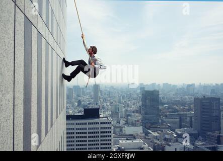 Geschäftsmann steigt mit einem Seil in ein hohes Gebäude. Konzept der Bestimmung Stockfoto