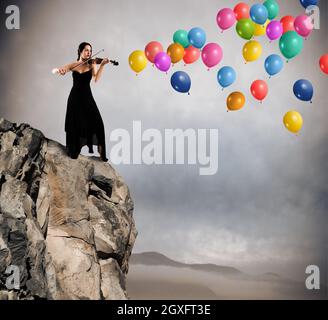 Geiger spielt auf einem Berg mit bunten Luftballons fliegen Stockfoto