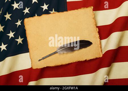 Nahaufnahme eines leeren gelben Papierblatts und einer Federkiel auf einem alten, verwitterten, mit US-Nationalflagge bestickten Baumwollhintergrund, Symbol der amerikanischen Geschichte, eleva Stockfoto