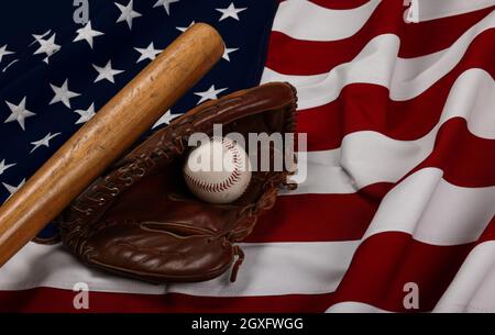 Nahaufnahme eines alten Baseballballs, eines hölzernen Bate und eines getragenen Vintage-Handschuhs aus Leder auf dem Hintergrund einer amerikanischen Flagge, aus einem hohen Winkel Stockfoto