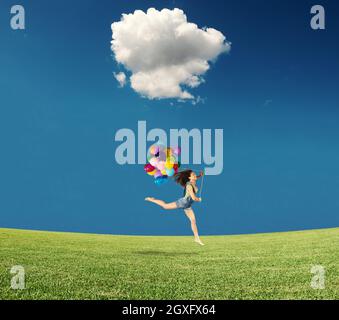 Mädchen springt mit farbigen Ballons in einem grünen Feld Stockfoto