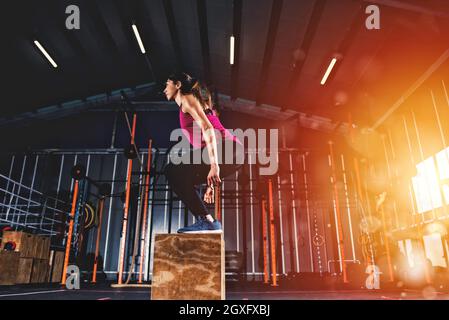 Entschlossenes athletisches Mädchen macht Boxsprungübungen im Fitnessstudio Stockfoto