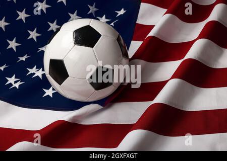 Nahaufnahme getragener schwarz-weißer Fußball-Fußball über dem Hintergrund der amerikanischen Flagge, Blick aus dem Hochwinkel Stockfoto