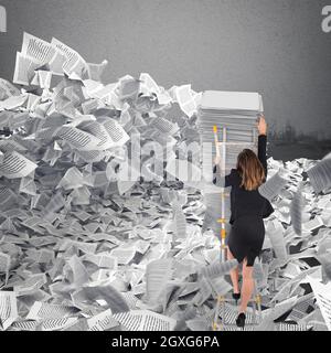 Geschäftsfrau mit Papierbogen überall im Büro. Begraben durch Bürokratiekonzept. Stockfoto