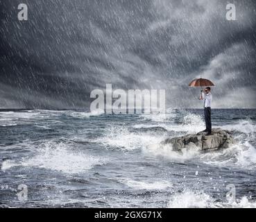 Geschäftsmann mit Regenschirm während Sturm im Meer. Konzept von Problem und Krise Stockfoto