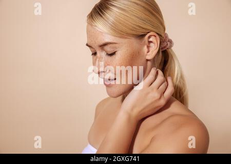 Porträt einer Frau mit Sommersprossen, die ihren Hals im Studio berühren Stockfoto