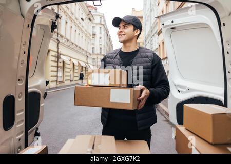Männlicher Kurier in Uniform, der am Kofferraum des Transporters steht und die Kisten für die Auslieferung an den Kunden bereithält Stockfoto