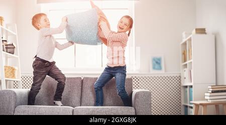 Niedliche Kinder kämpfen mit Kissen auf dem Sofa. Konzept der Freundschaft und Beziehung in der Familie. Stockfoto