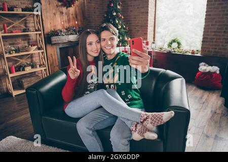 Foto-Porträt junger Mann in hässlichen Pullover, Selfie mit Freundin zeigt V-Zeichen auf der Couch Stockfoto