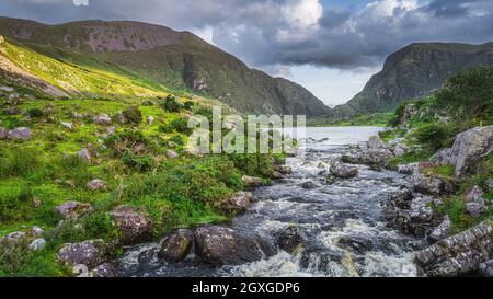 Gebirgsfluss, der vom Black Lake in Gap of Dunloe fließt. Grüne Hügel bei Sonnenuntergang im Black Valley, MacGillycuddys Reeks Mountains, Ring of Kerry, Irland Stockfoto