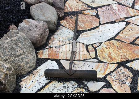 Ein Rechen wird verwendet, um schwarze Kieselsteine zwischen Terrassensteinen zu platzieren. Stockfoto