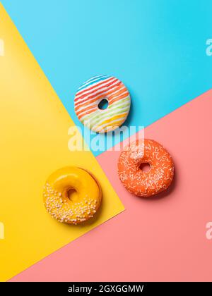 Kreatives Layout aus köstlichen glasierten Donuts. Vertikale flache Lay - Donuts oder Donuts auf buntem Hintergrund mit Kopierraum. Blau, gelb und pi Stockfoto