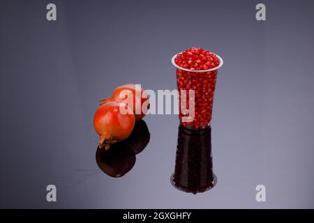 Frischer Granatapfelkern, in einem Glas mit frischem Obst angeordnet, daneben auf grauem Hintergrund, isoliert. Stockfoto