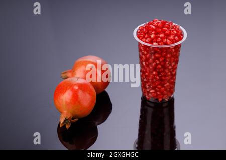 Frischer Granatapfelkern, in einem Glas mit frischem Obst angeordnet, daneben auf grauem Hintergrund, isoliert. Stockfoto