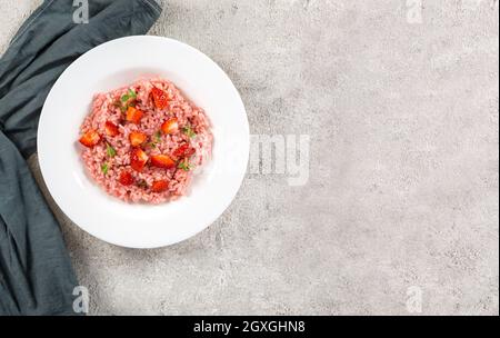 Risotto mit Erdbeerfrüchten serviert in einem weißen Gericht auf einem grauen Steintisch. Flach liegend mit Kopierraum. Italienische Gourmetküche. Selektiver Fokus. Stockfoto