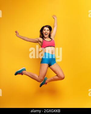 Bestimmte Sportfrau springt auf einem gelben Hintergrund. Fröhlicher und freudiger Ausdruck. Stockfoto