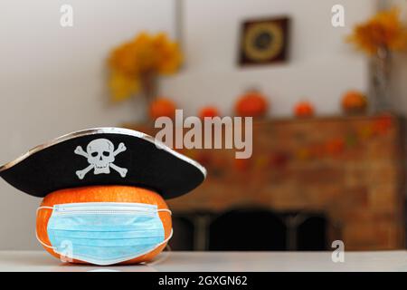 Halloween Kürbis mit einem Piratenhut in einer Schutzmaske auf dem Tisch vor dem Hintergrund eines Wohnkamins mit Herbstdekorationen. Stockfoto
