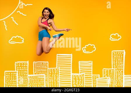 Determined Sport Frau springt auf einem gelben Hintergrund mit Wolkenkratzern Zeichnung. Fröhlicher und freudiger Ausdruck. Stockfoto