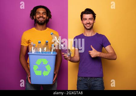 Glückliche Freunde halten einen Plastikbehälter mit Flaschen gelb und lila Farbe. Konzept der Ökologie, Konservierung, Recycling und Nachhaltigkeit Stockfoto