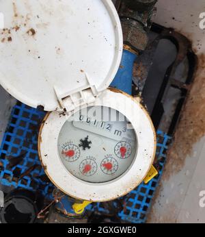 Wasserzähler. Rostiger und schmutziger Wasserzähler für den Außenbereich zur Messung des Wasserdurchflusses. Draufsicht des Wasserzählers mit geöffneter Abdeckung. Stockfoto