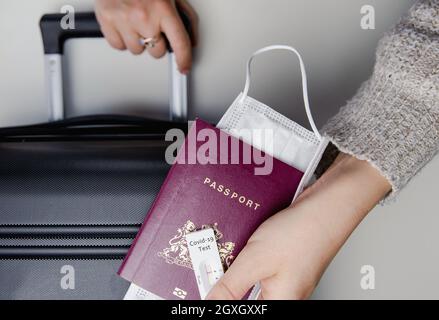 COVID-19, Reise- und Lockdown-Konzept, Junge Frauen Hand mit Pass, medizinische Maske und negativen Schnelltest Coronavirus und Koffer, Reisen, requireme Stockfoto