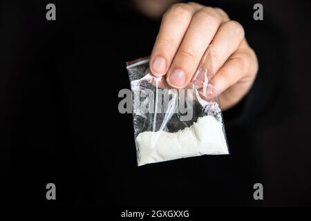 Drogenhändler, der Drogen in einer Plastiktüte, Kokain, Heroin, Geschwindigkeit oder andere Drogen auf dunkelschwarzem Hintergrund, sucht, Drogen, klobig, kriminelle Konzeptkopien gibt Stockfoto