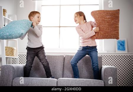 Niedliche Kinder kämpfen mit Kissen auf dem Sofa. Konzept der Freundschaft und Beziehung in der Familie. Stockfoto