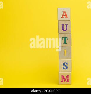 Holzwürfel mit der Aufschrift Autismus auf gelbem Hintergrund. Konzept der Unterstützung und Ermutigung für Kinder mit Entwicklungsstörungen des Stockfoto