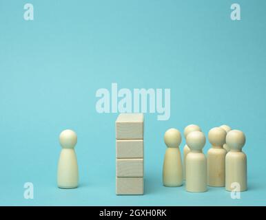 Holzfiguren von Männern die Menge steht vor einer Wand aus Holzblöcken, auf der anderen Seite eine Figur. Das Konzept eines Streits und Missverständnisse Stockfoto