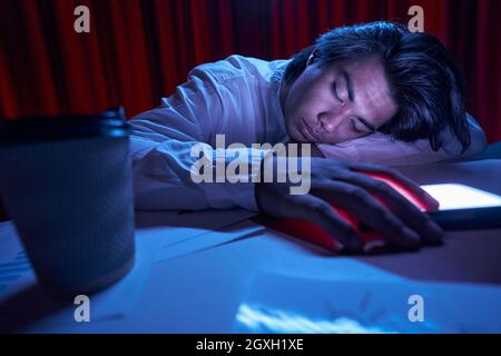 Müde Angestellte, die am Abend am Arbeitsplatz schlafen Stockfoto