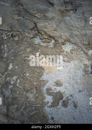 Verwitterte und rissige Betonwand mit blauem Kalk und verschiedenen Mörtelmischungen im Laufe der Zeit erhalten. Abblätternder Putz von der Oberfläche der Zementstruktur. Stockfoto